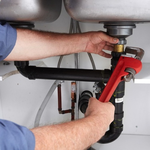 close-up of a plumber fixing pipes under a sink